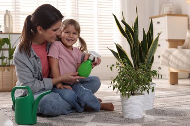 Photo of Little helper. Mother and her cute daughter with spray bottle near houseplants at home