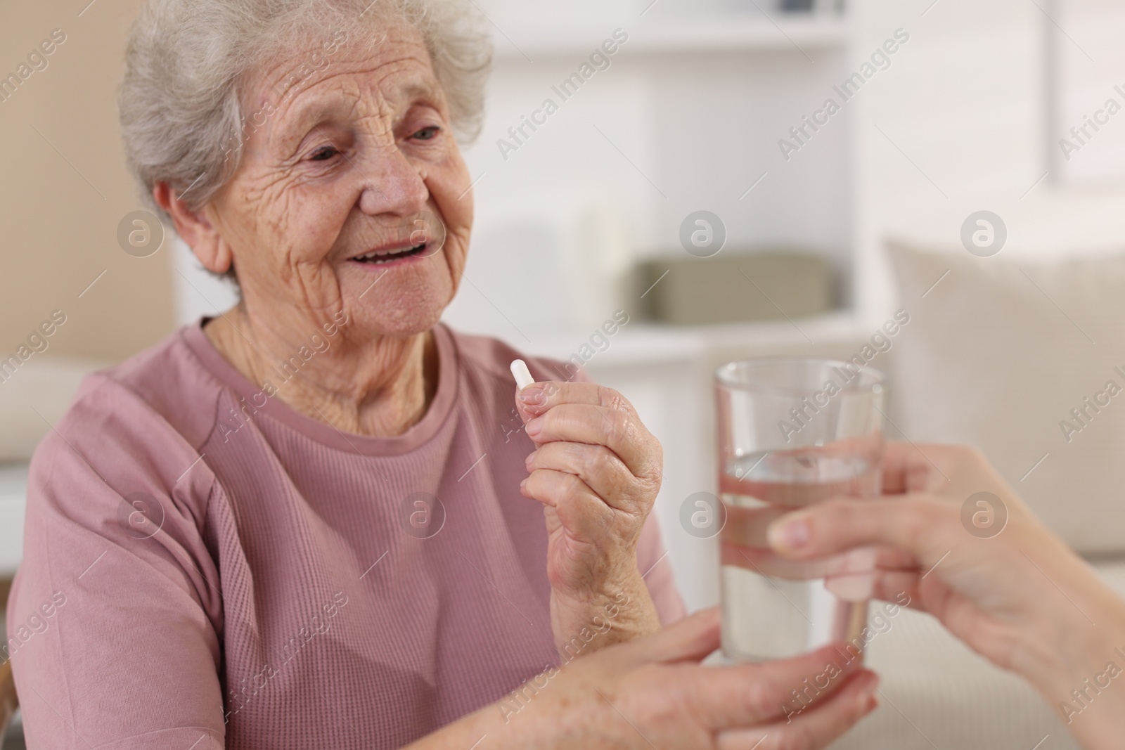 Photo of Caregiver giving glass of water to smiling senior woman with medical pill indoors, closeup