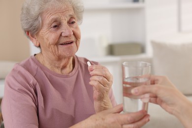 Photo of Caregiver giving glass of water to smiling senior woman with medical pill indoors, closeup