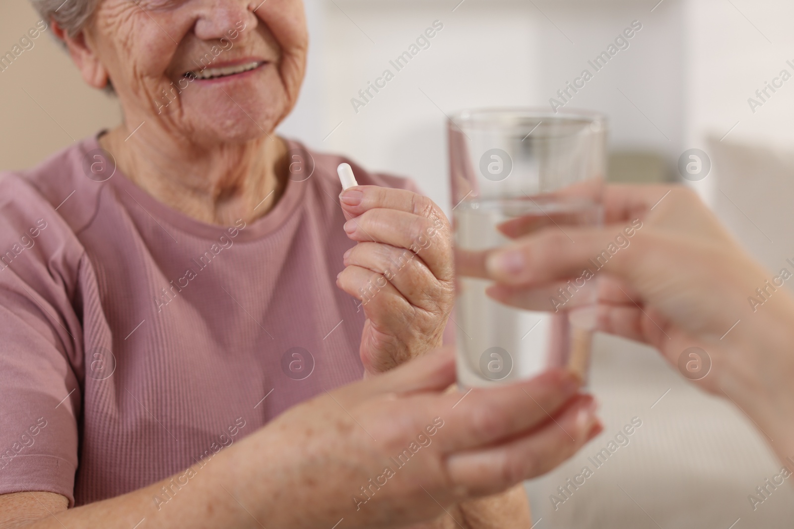 Photo of Caregiver giving glass of water to smiling senior woman with medical pill indoors, closeup