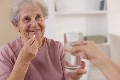 Photo of Caregiver giving glass of water to smiling senior woman with medical pill indoors, closeup