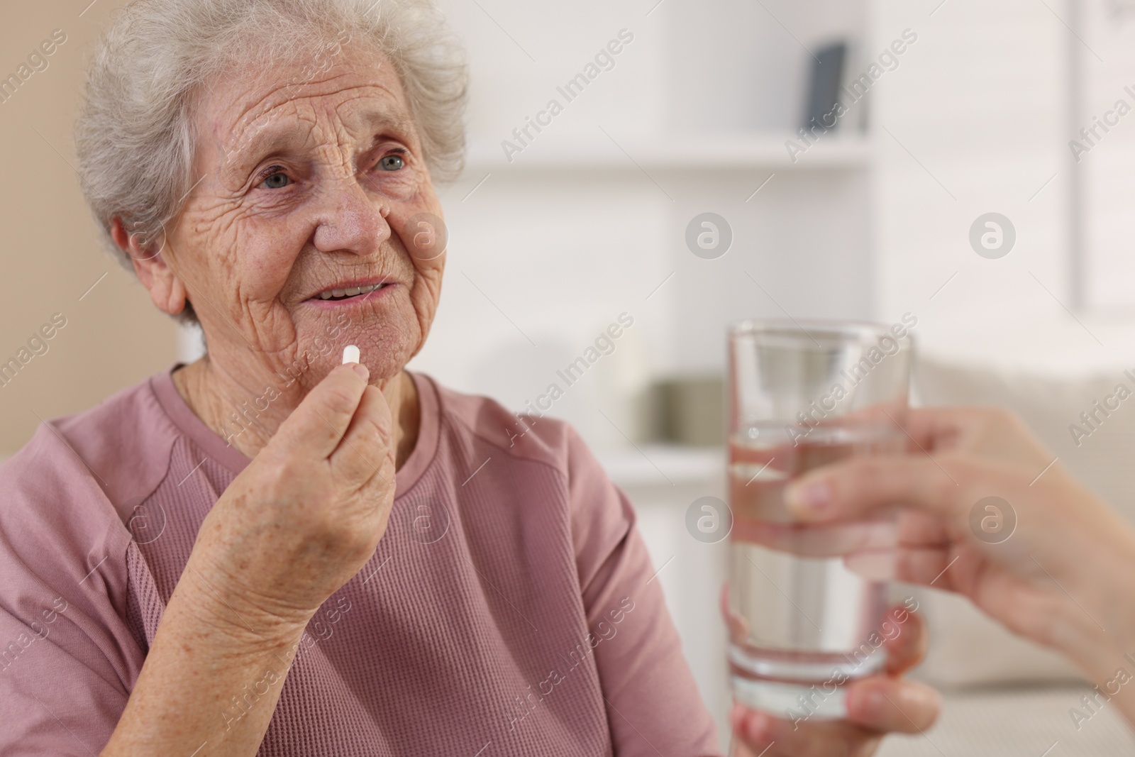 Photo of Caregiver giving glass of water to smiling senior woman with medical pill indoors, closeup