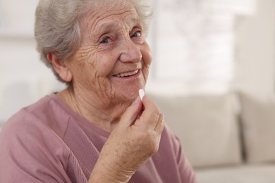 Photo of Smiling senior woman taking medical pill at home, closeup. Space for text