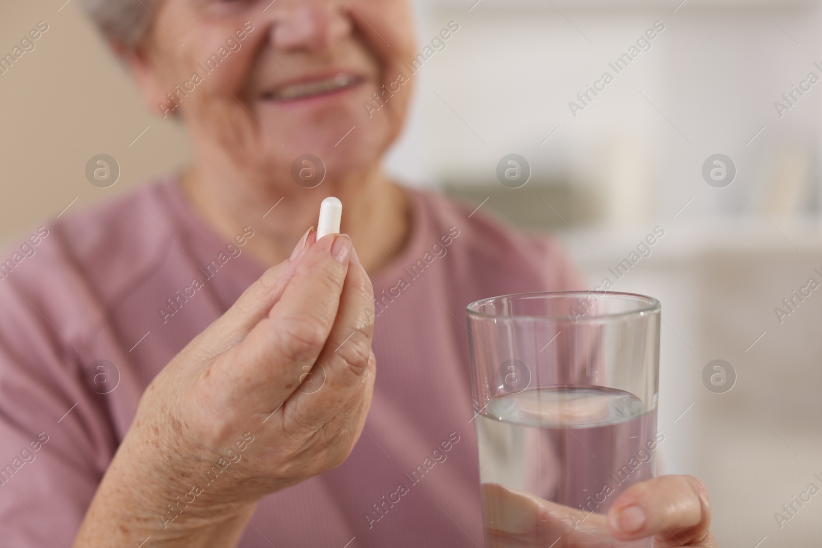 Photo of Senior woman with glass of water and pill at home, selective focus