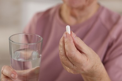 Photo of Senior woman with glass of water and pill at home, closeup