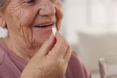 Photo of Senior woman with glass of water taking pill at home, closeup. Space for text