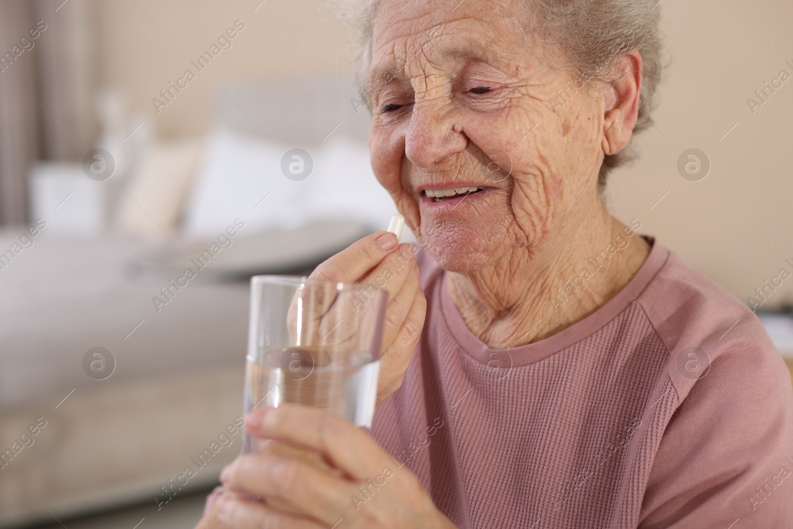 Photo of Smiling senior woman with glass of water taking pill at home, closeup. Space for text