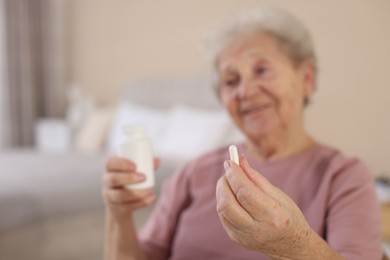 Photo of Senior woman with medical pill and bottle at home, selective focus