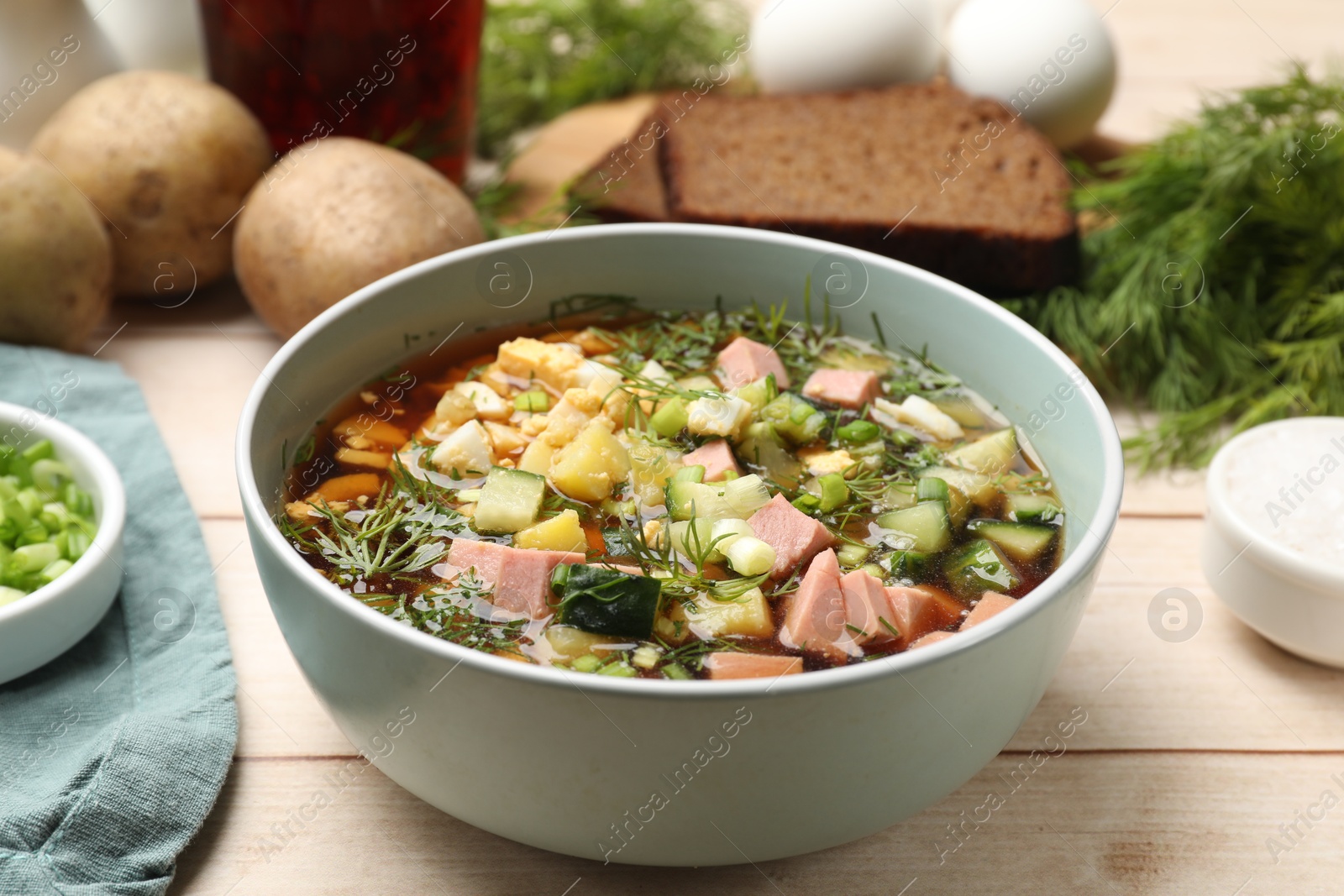 Photo of Delicious okroshka soup with kvass and ingredients on white wooden table, closeup