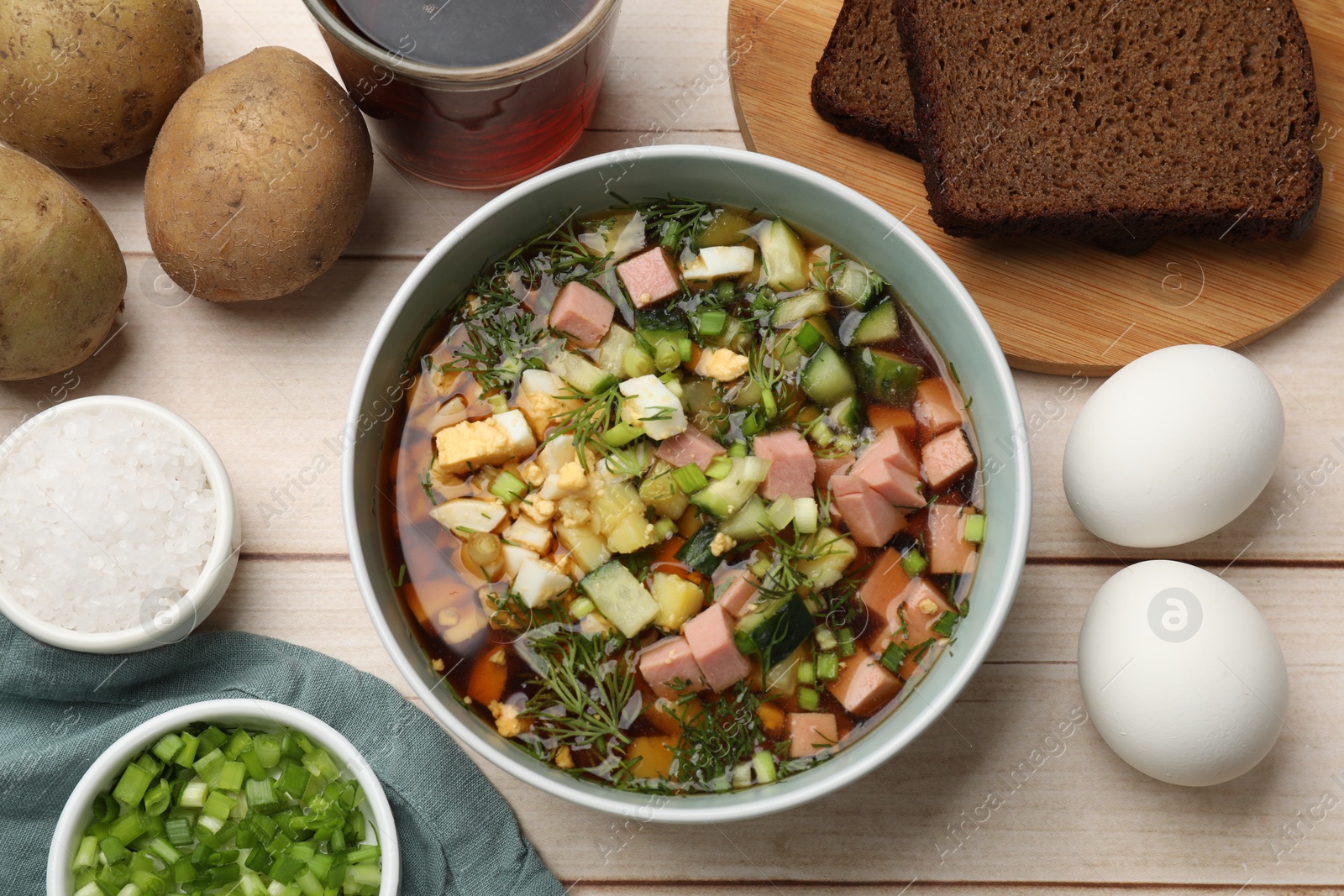 Photo of Delicious okroshka soup with kvass and ingredients on white wooden table, flat lay