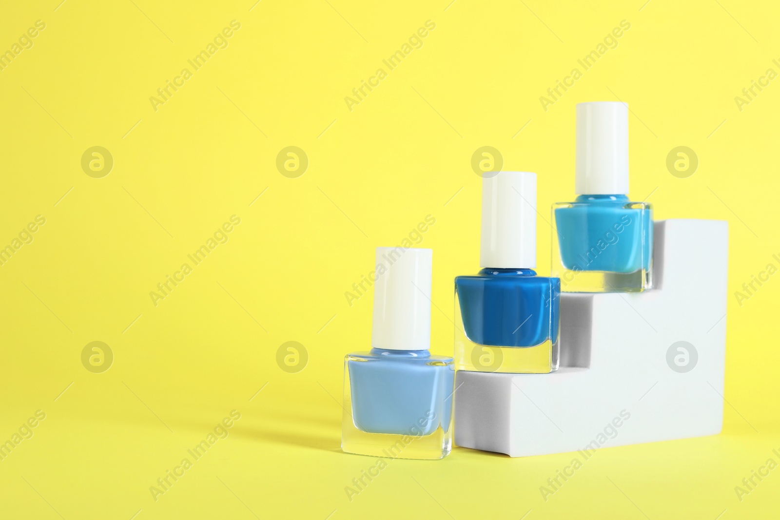 Photo of Stylish presentation of nail polishes in bottles on yellow background. Space for text