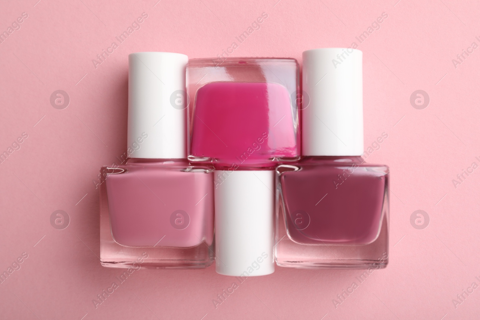 Photo of Set of different nail polishes in bottles on pink background, flat lay