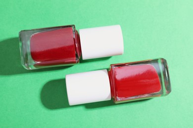 Photo of Red nail polishes in bottles on green background, flat lay