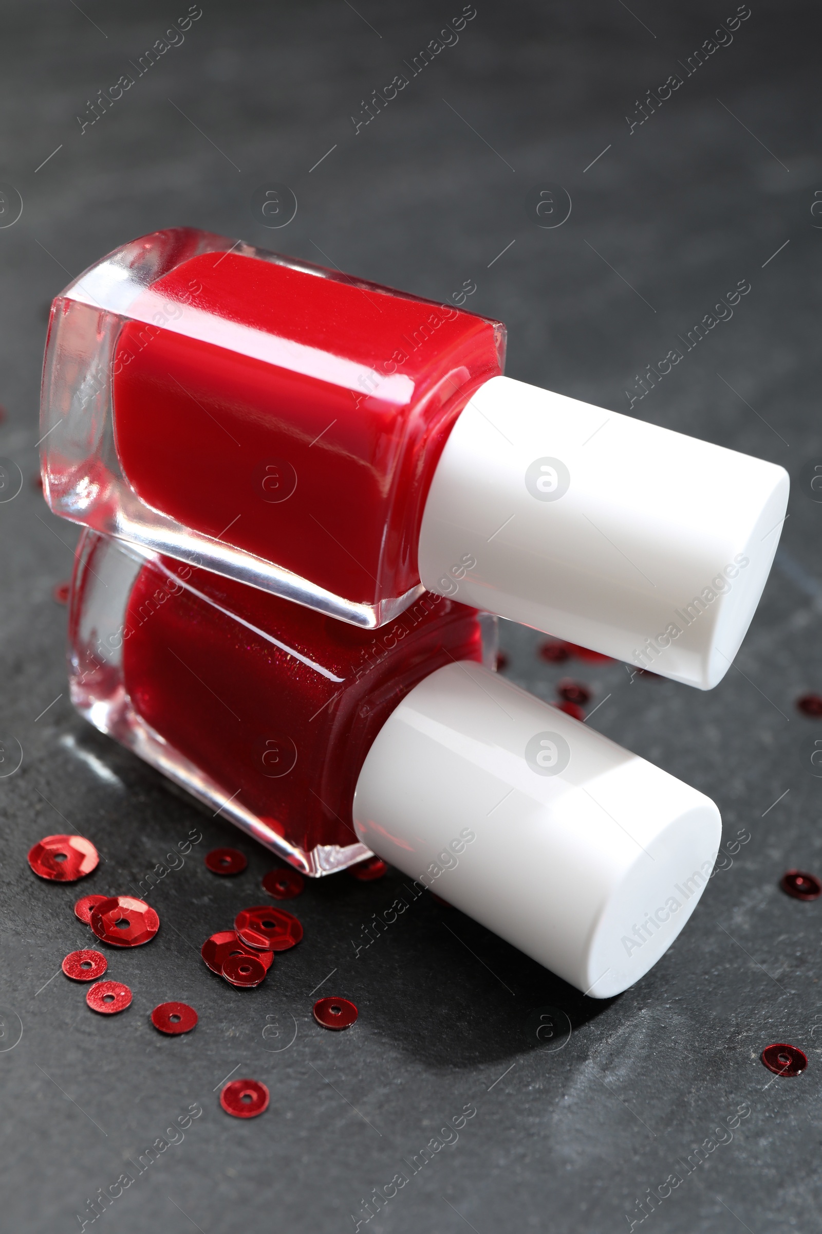 Photo of Red nail polishes in bottles on dark textured table, closeup