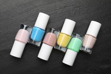 Photo of Set of different nail polishes in bottles on dark textured table, flat lay