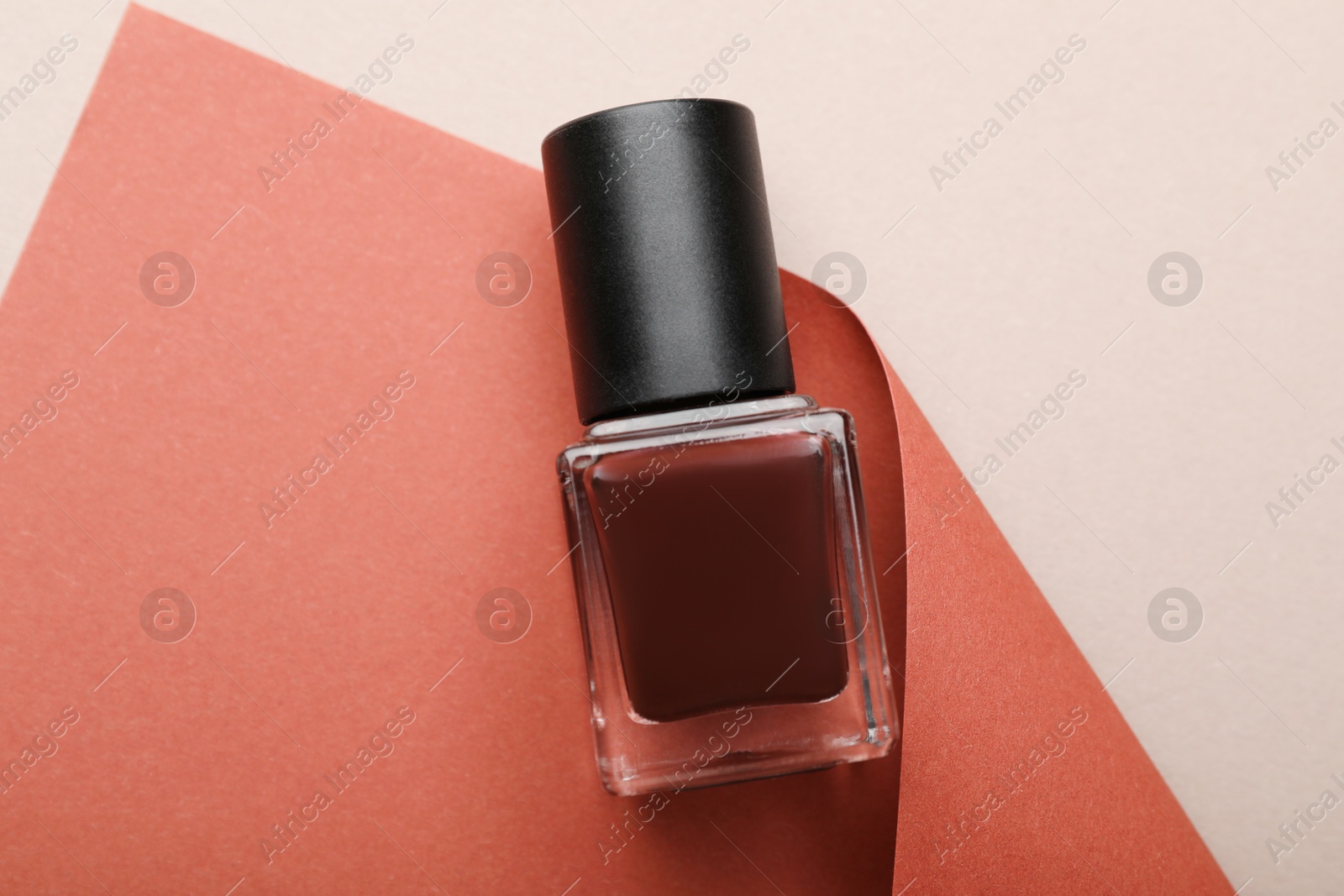 Photo of Nail polish in bottle and color paper on beige background, above view