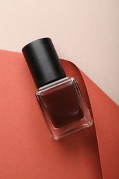 Photo of Nail polish in bottle and color paper on beige background, top view