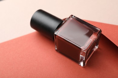 Photo of Nail polish in bottle and color paper on beige background, closeup