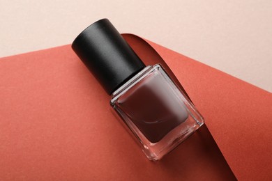 Photo of Nail polish in bottle and color paper on beige background, top view