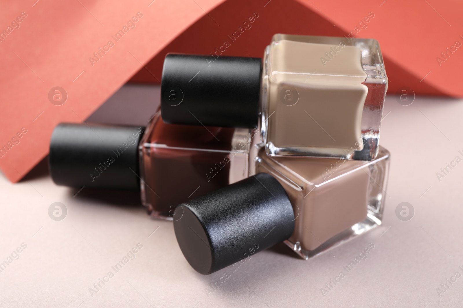 Photo of Nail polishes in bottles and color paper on beige background, closeup