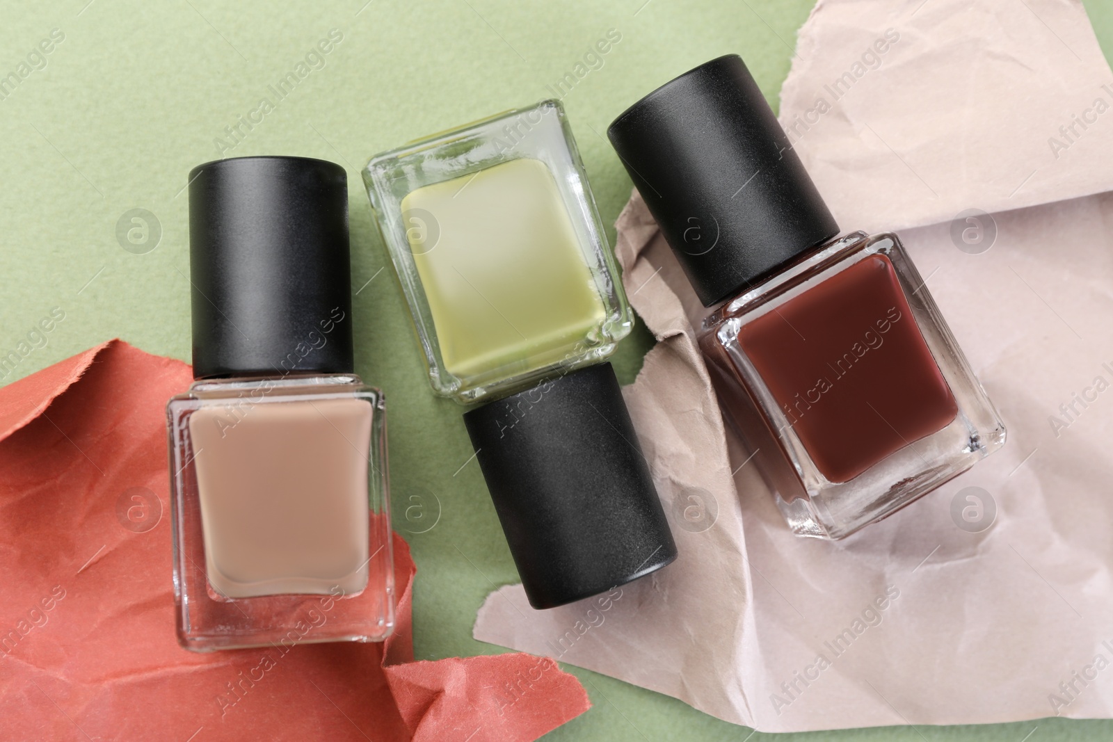 Photo of Nail polishes in bottles and craft paper on olive background, flat lay