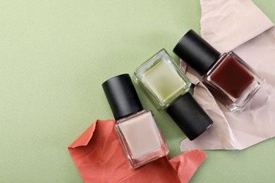 Photo of Nail polishes in bottles and craft paper on olive background, flat lay. Space for text