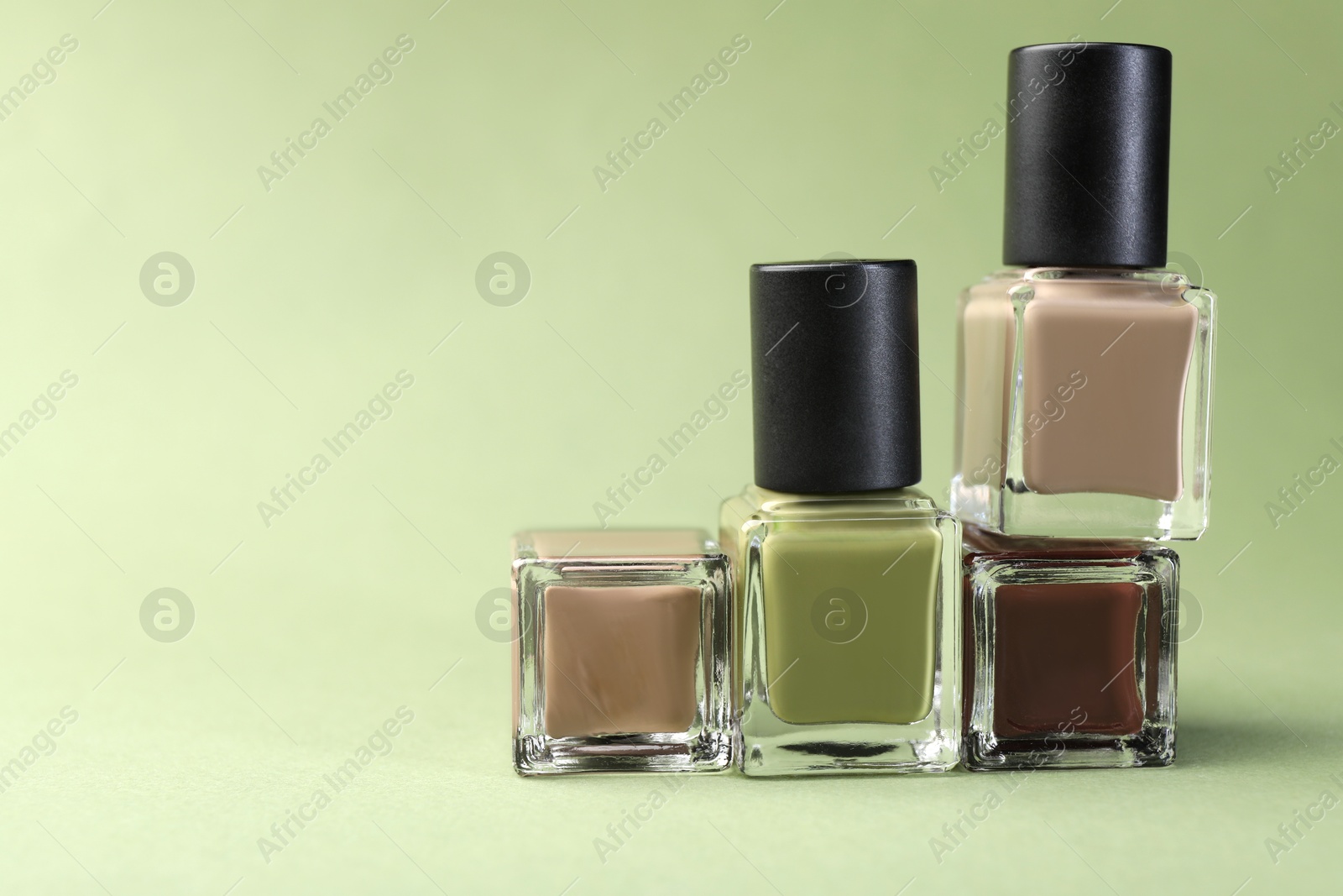 Photo of Nail polishes in bottles on olive background, space for text