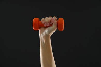 Photo of Woman exercising with dumbbell on black background, closeup