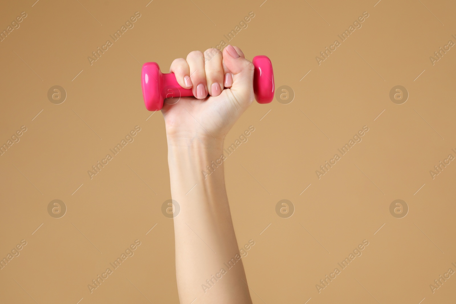 Photo of Woman exercising with dumbbell on beige background, closeup