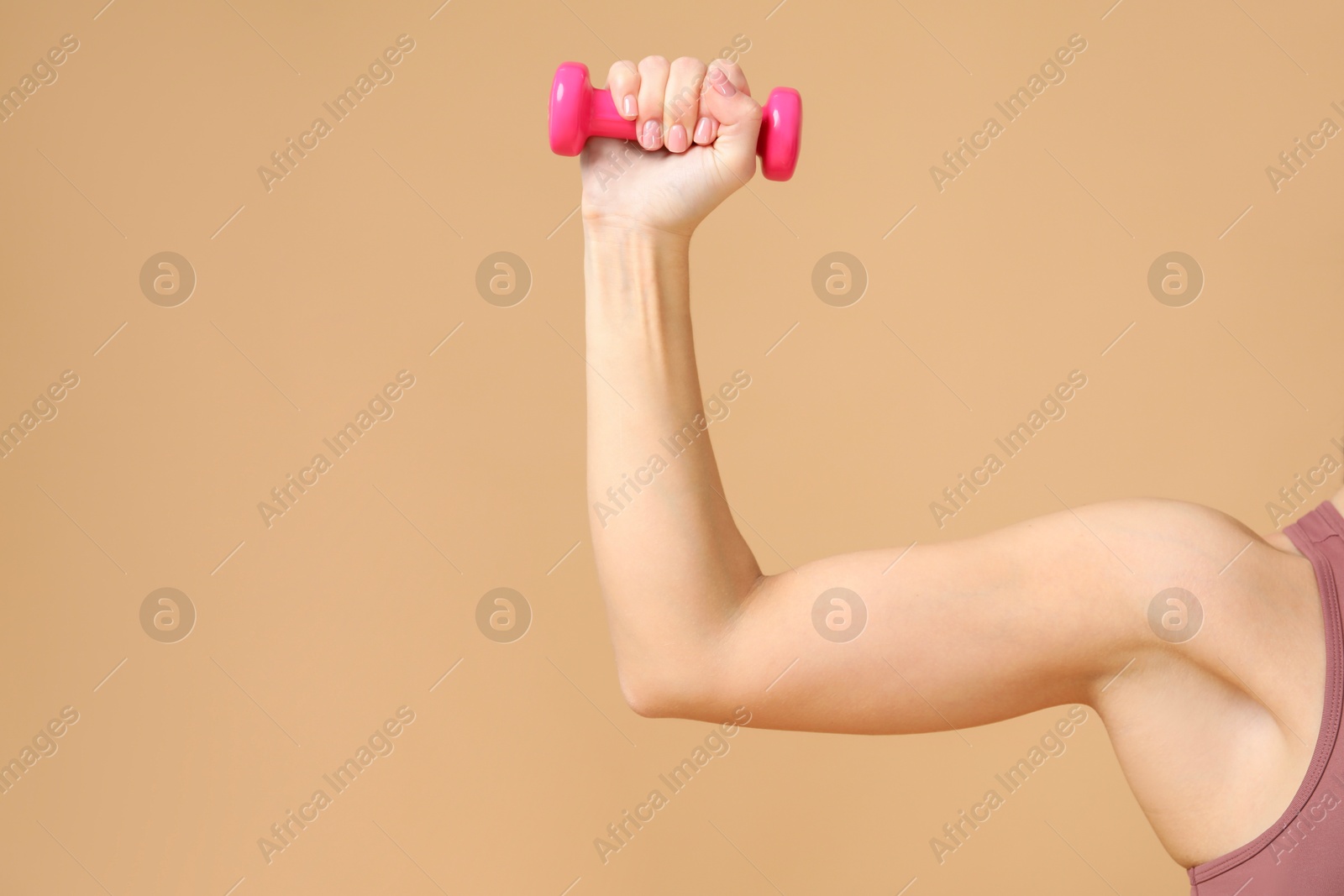 Photo of Woman exercising with dumbbell on beige background, closeup. Space for text