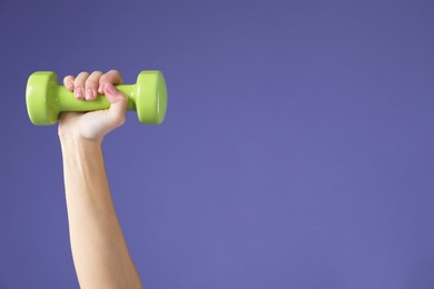 Photo of Woman exercising with dumbbell on purple background, closeup. Space for text