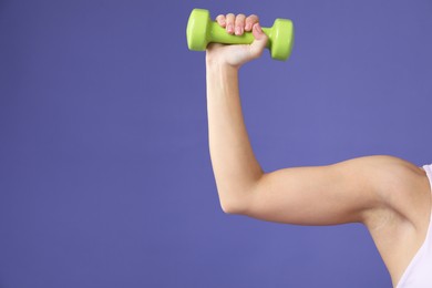 Photo of Woman exercising with dumbbell on purple background, closeup. Space for text