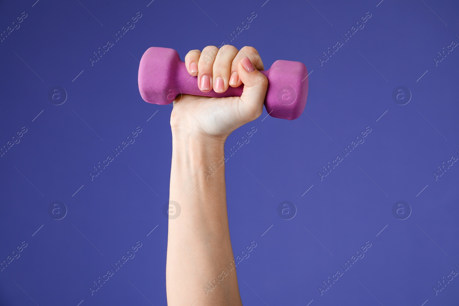 Photo of Woman exercising with dumbbell on purple background, closeup