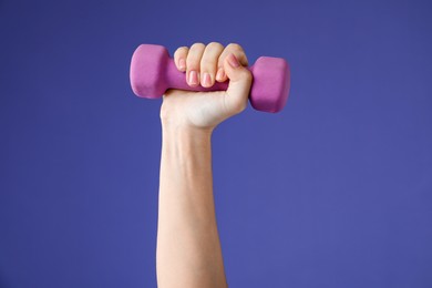 Photo of Woman exercising with dumbbell on purple background, closeup