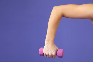 Photo of Woman exercising with dumbbell on purple background, closeup. Space for text