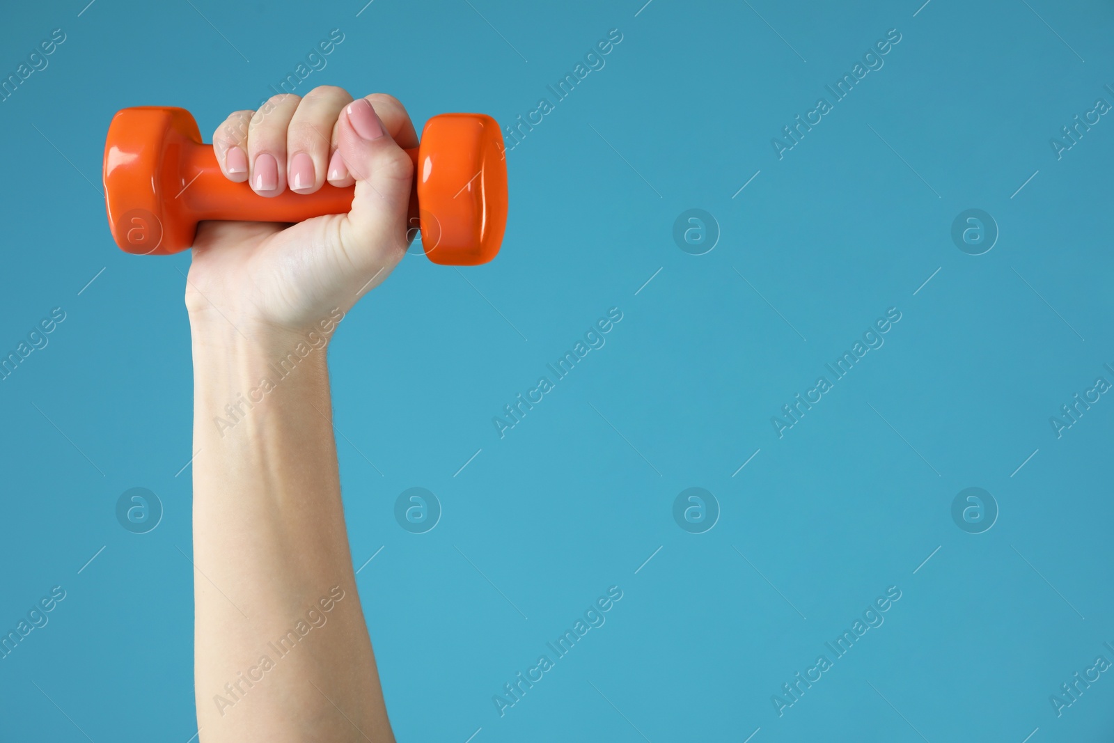 Photo of Woman exercising with dumbbell on light blue background, closeup. Space for text