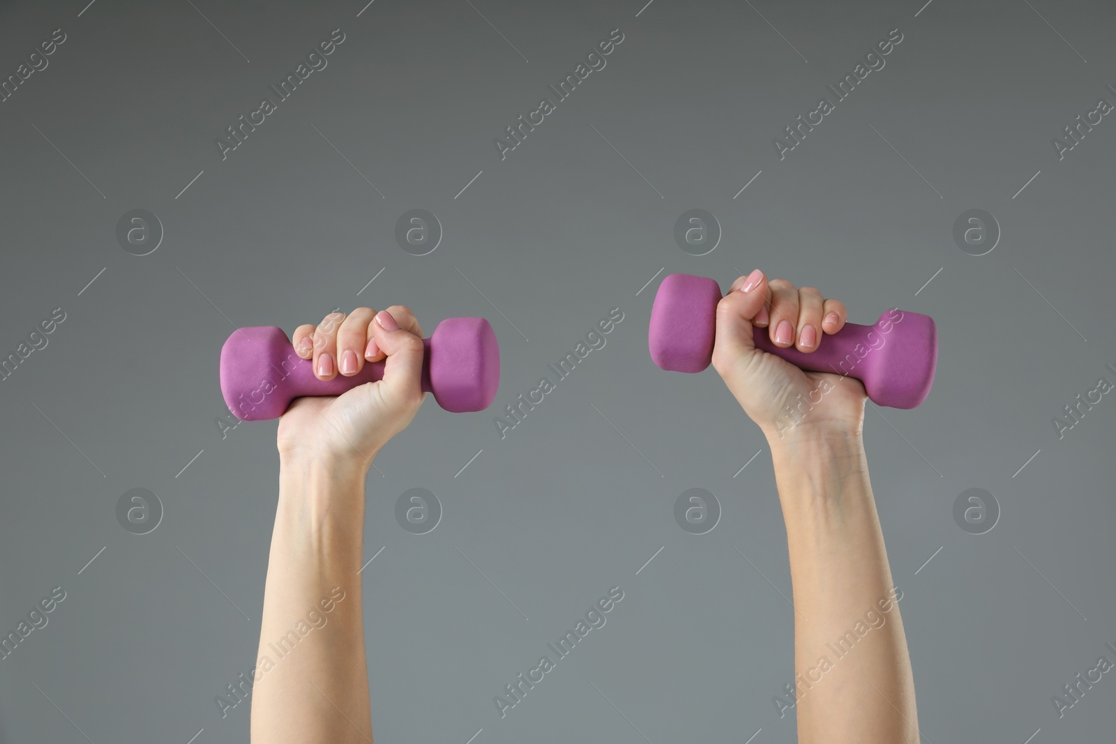 Photo of Woman exercising with dumbbells on light grey background, closeup