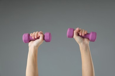 Woman exercising with dumbbells on light grey background, closeup