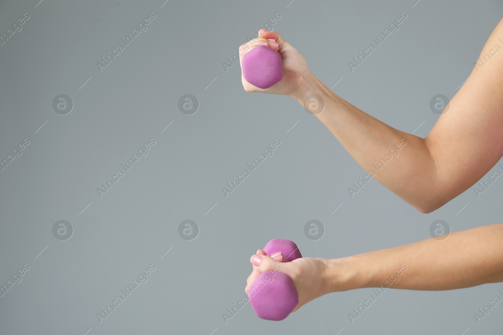 Photo of Woman exercising with dumbbells on light grey background, closeup. Space for text