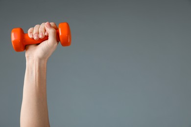 Woman exercising with dumbbell on light grey background, closeup. Space for text