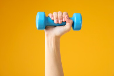 Photo of Woman exercising with dumbbell on orange background, closeup