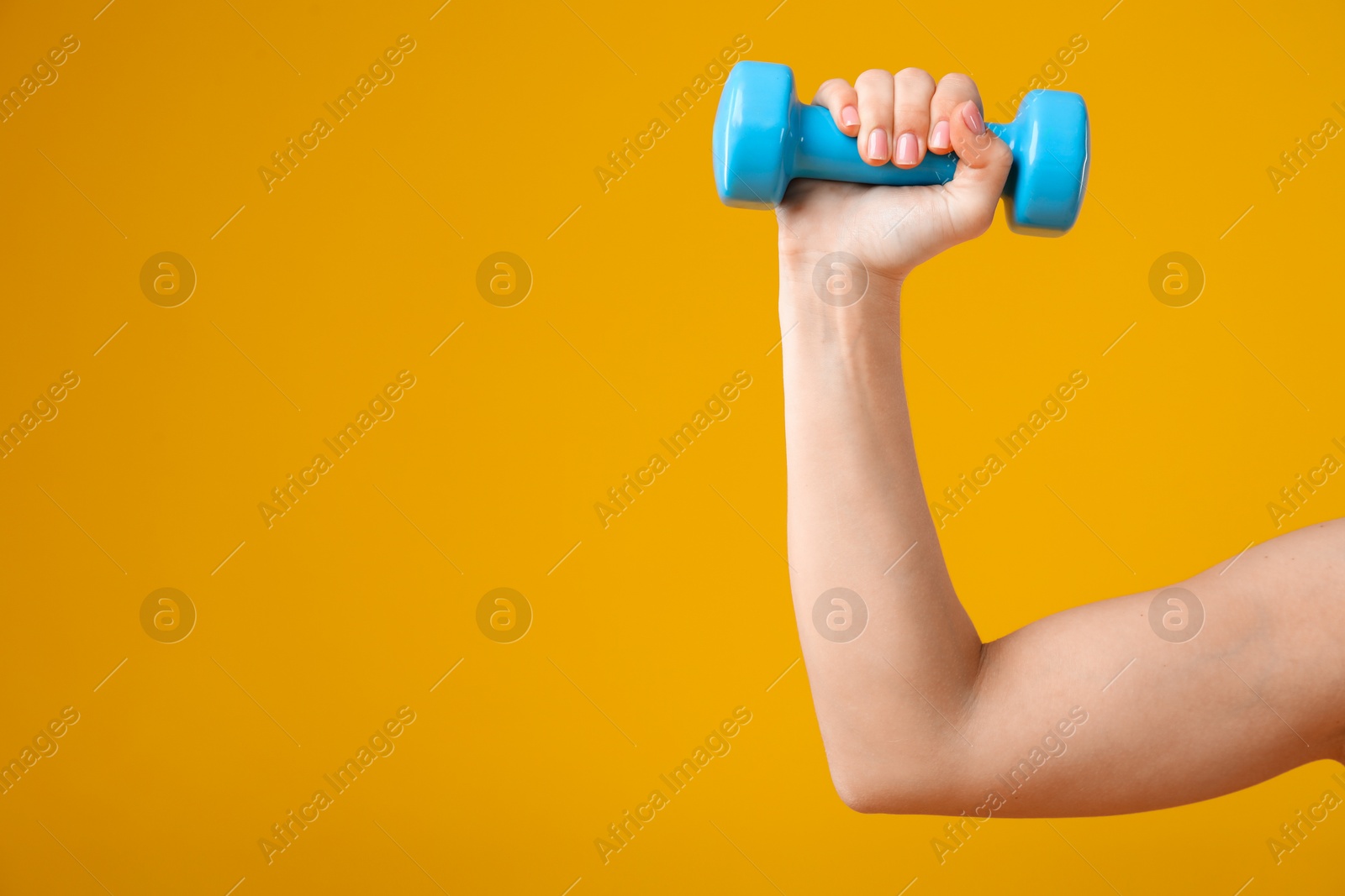 Photo of Woman exercising with dumbbell on orange background, closeup. Space for text