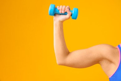 Photo of Woman exercising with dumbbell on orange background, closeup. Space for text