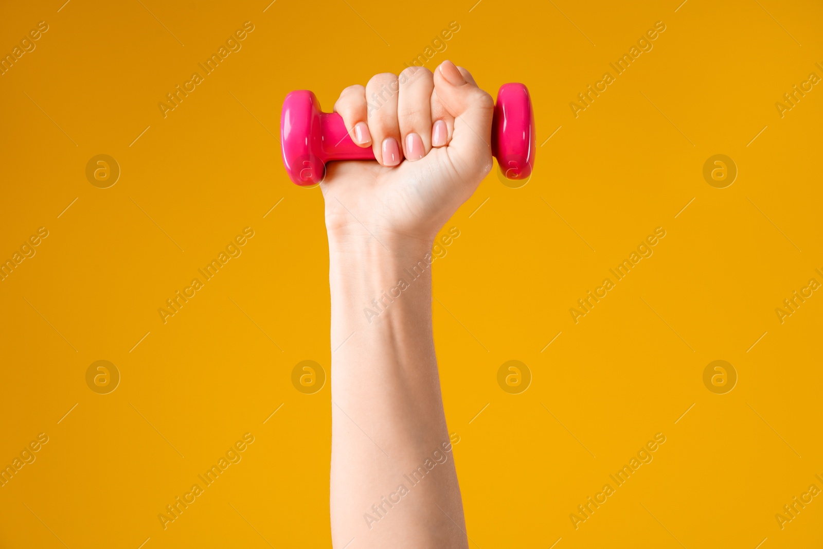 Photo of Woman exercising with dumbbell on orange background, closeup