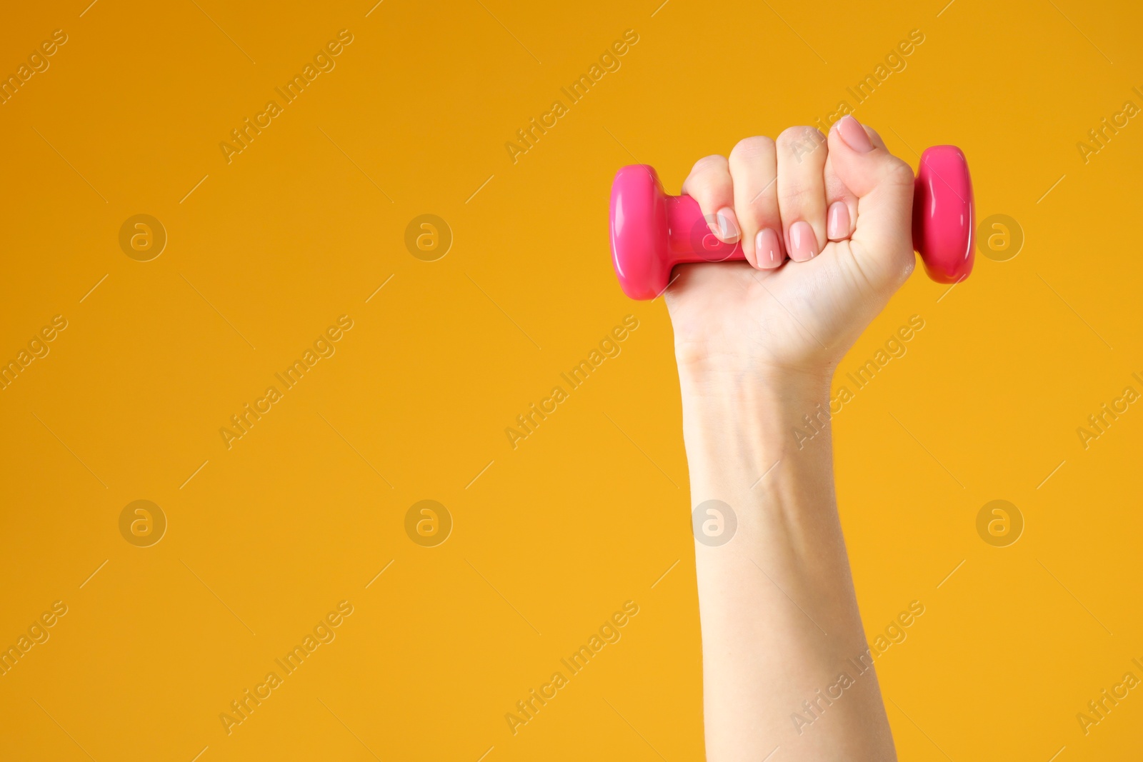 Photo of Woman exercising with dumbbell on orange background, closeup. Space for text