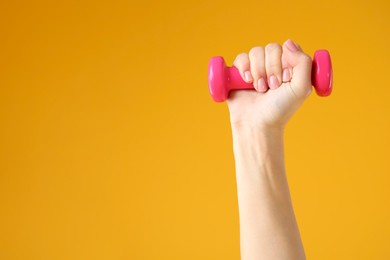 Photo of Woman exercising with dumbbell on orange background, closeup. Space for text