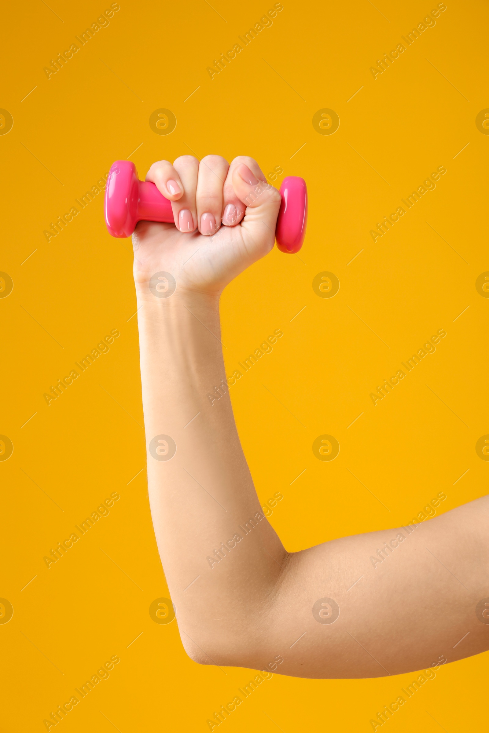 Photo of Woman exercising with dumbbell on orange background, closeup