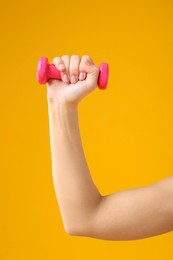 Woman exercising with dumbbell on orange background, closeup