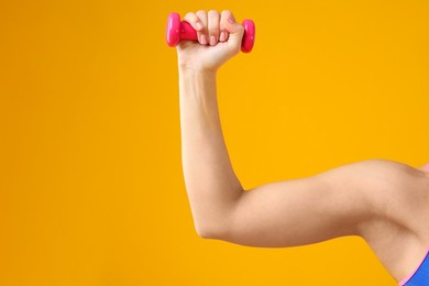 Woman exercising with dumbbell on orange background, closeup. Space for text