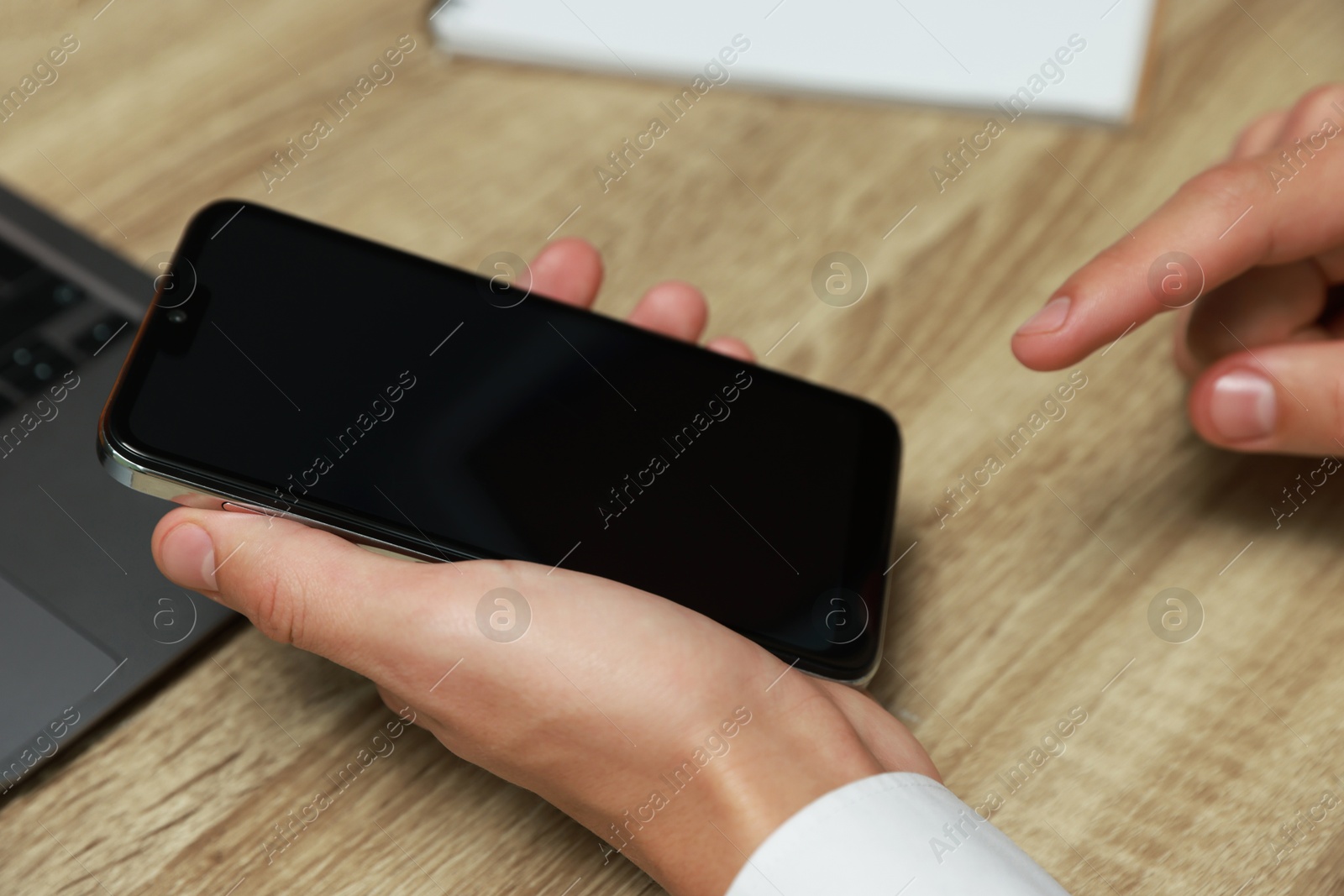 Photo of Man using smartphone with blank screen at wooden table, closeup